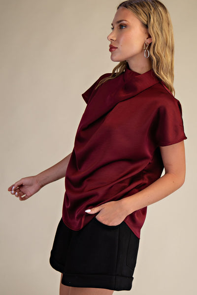 Woman wearing a burgundy top with a draped design on a beige background