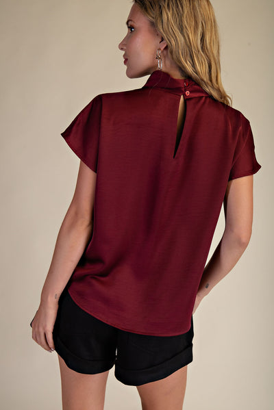 Woman wearing a burgundy blouse and black shorts on a beige background