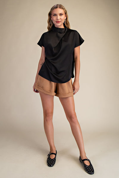Woman wearing a black top and beige shorts on a beige background