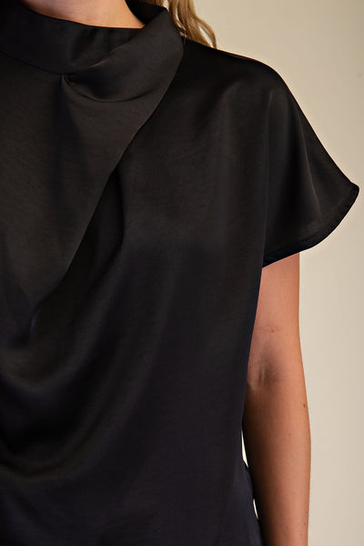Black cowl-neck top worn by a person on a beige background
