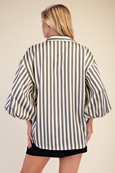 A woman shown from the back wearing an oversized button-up shirt with vertical grey and off-white stripes, paired with black shorts, against a solid beige background.
