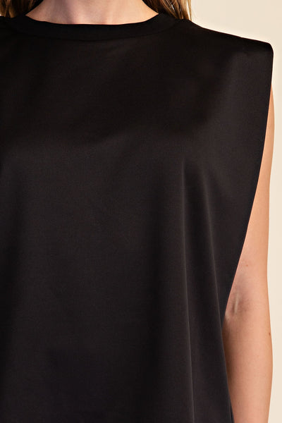 Close-up of a person wearing a black sleeveless top with a wide crew neckline and draped fabric.