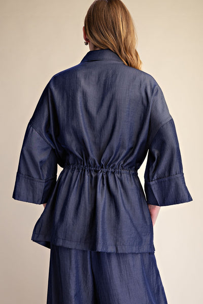 A woman shown from the back wearing a dark blue top and matching pants against a plain beige studio background.