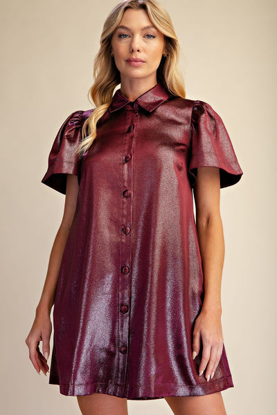 A woman modeling a short-sleeve collared shirt dress in a shiny burgundy fabric, set against a plain beige background.