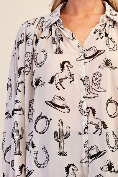 A close-up of a woman wearing a long-sleeve button-up shirt with a western-themed black print featuring cacti, horseshoes, cowboy boots, hats, and horses on a light beige background.