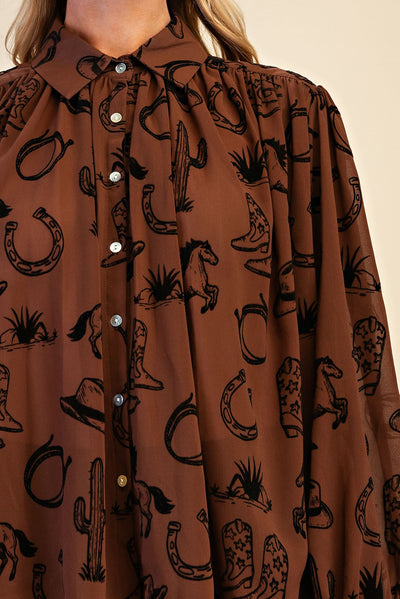 A close-up of a brown button-up shirt with a black western-themed print featuring horseshoes, cowboy boots, cacti, and horses, worn by a model.
