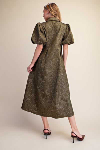 A woman modeling a mid-length olive green dress with a textured leaf-like pattern, puffed short sleeves, and a collar, shown from the back against a plain beige studio background.