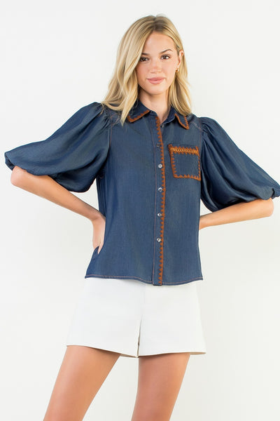 Woman wearing a blue blouse with brown trim on a white background