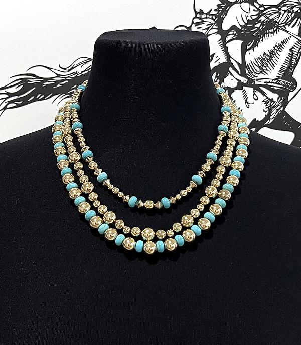 Necklace with turquoise and gold beads on a black stand against a black background