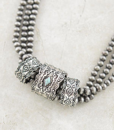 Silver beaded necklace with ornate rings on a textured white background