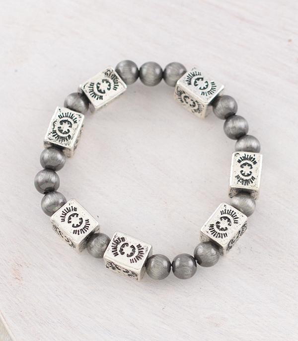 Gray beaded bracelet with silver square charms on a light wooden surface