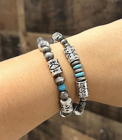 Two bracelets with silver and turquoise beads on a wrist against a blurred background
