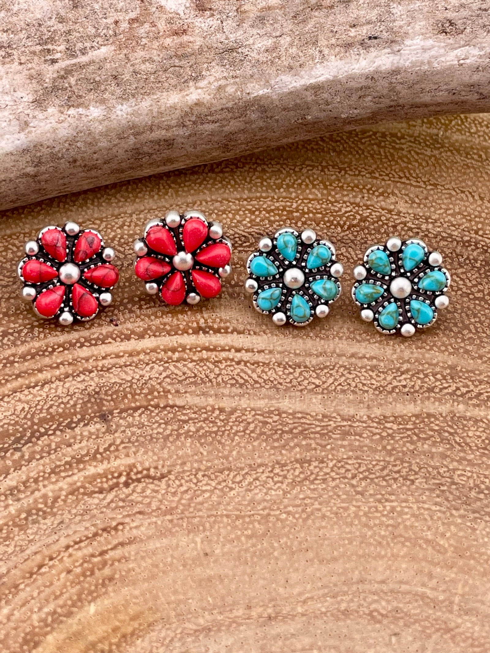 Pair of flower-shaped earrings with red and turquoise stones on a wooden surface