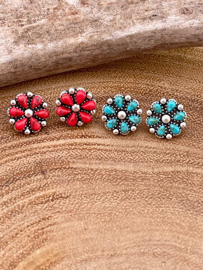 Pair of flower-shaped earrings with red and turquoise stones on a wooden surface