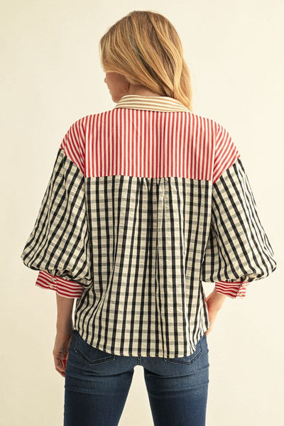 A woman shown from the back wearing a color-block blouse with a red and white striped yoke, a black and white gingham body, and red and white striped cuffs, paired with blue jeans against a plain cream background.
