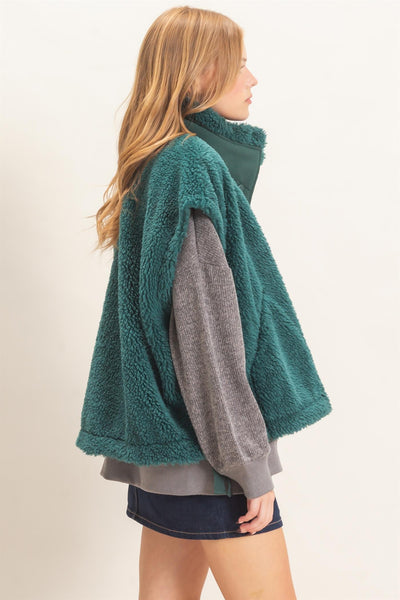 side view of a model wearing a gray shirt and jeans skirt with a green Sherpa Vest over it.