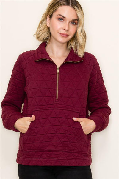 Woman wearing a burgundy quilted pullover against a plain background