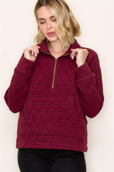 Woman wearing a burgundy quilted pullover against a plain background