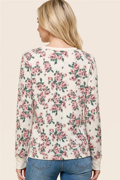A woman shown from the back wearing a cream-colored long-sleeve top with a pink rose floral pattern and blue jeans, set against a solid light beige background.