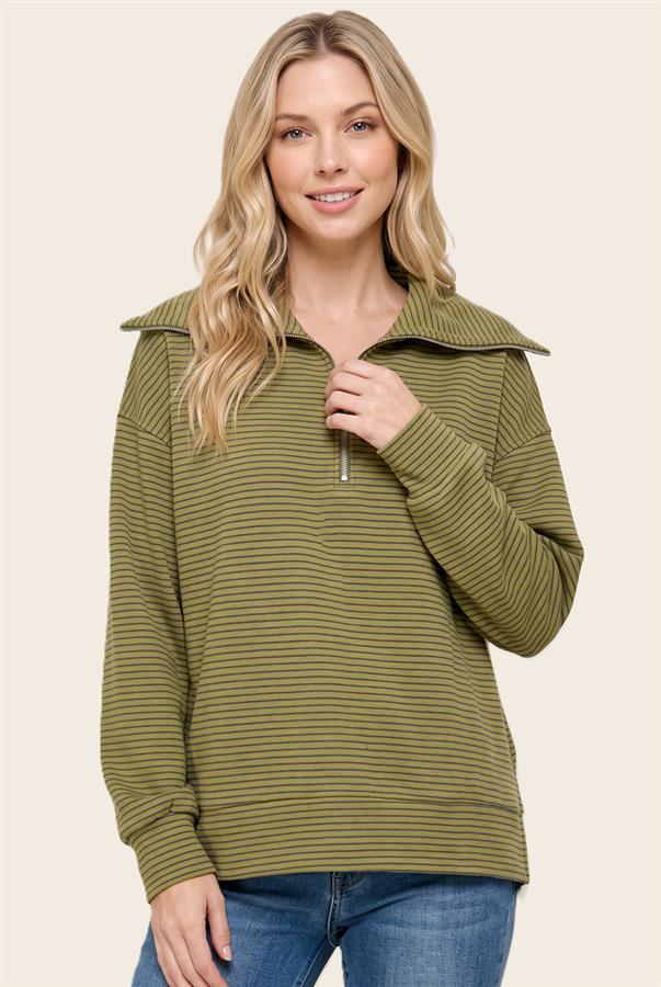 A woman wearing a green and olive striped long-sleeve quarter-zip pullover sweater with a wide collar, paired with blue jeans, against a solid beige background.