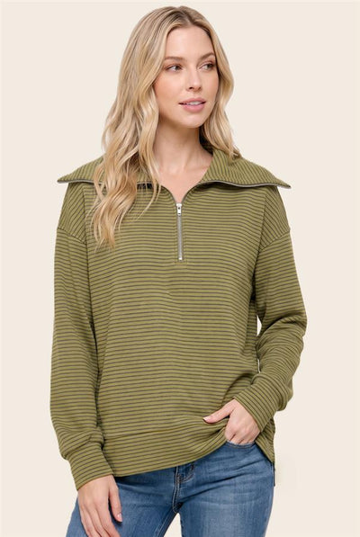 A woman modeling a long-sleeve olive green and dark green striped quarter-zip pullover with a wide collar, paired with blue jeans, against a solid light beige background.