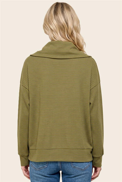 A woman viewed from the back wearing an olive green and dark green horizontally striped long-sleeve cowl neck top, paired with blue jeans, against a solid light beige background.