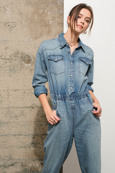 Person wearing a denim jumpsuit against a textured wall.