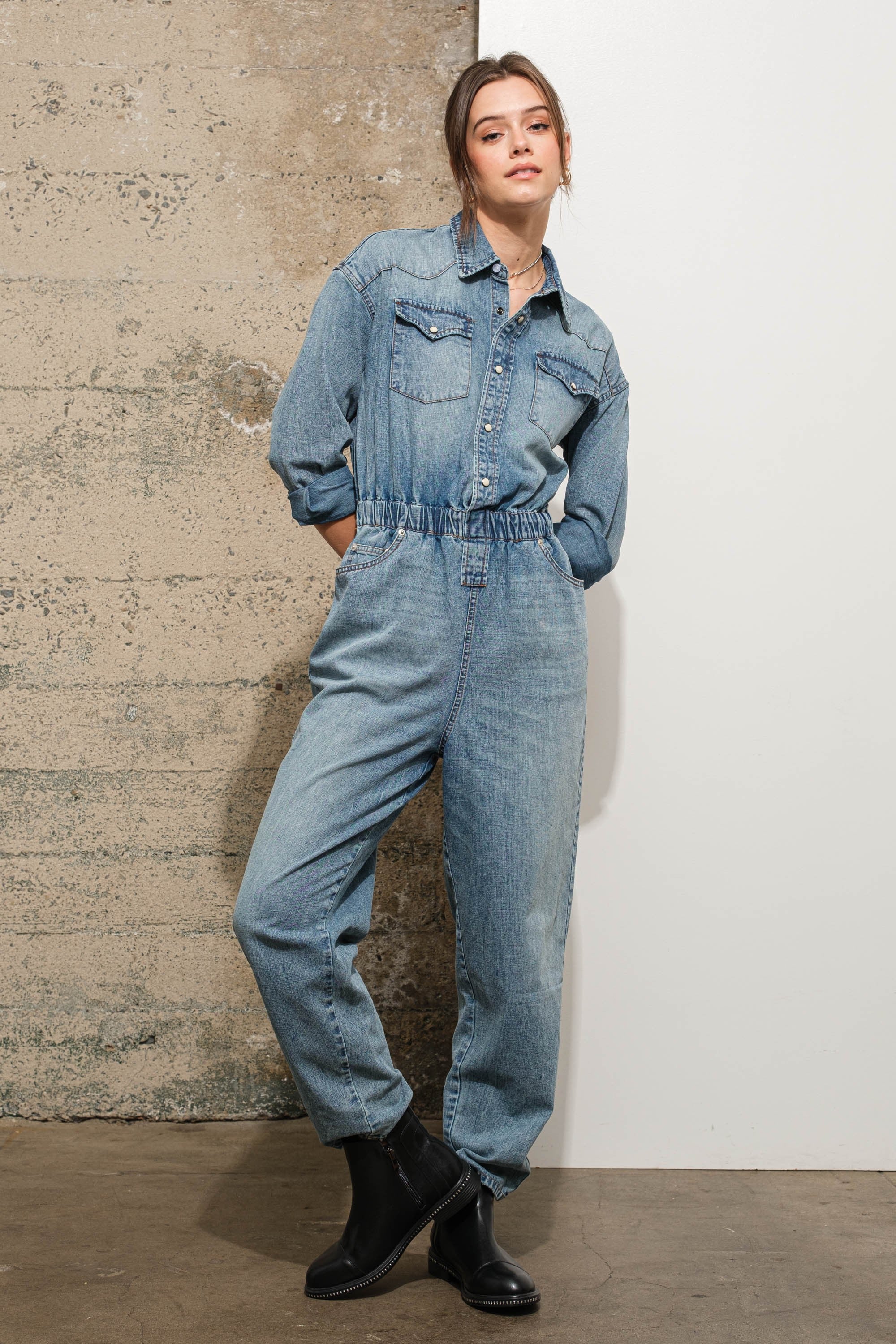 Person wearing a denim jumpsuit standing against a textured wall.