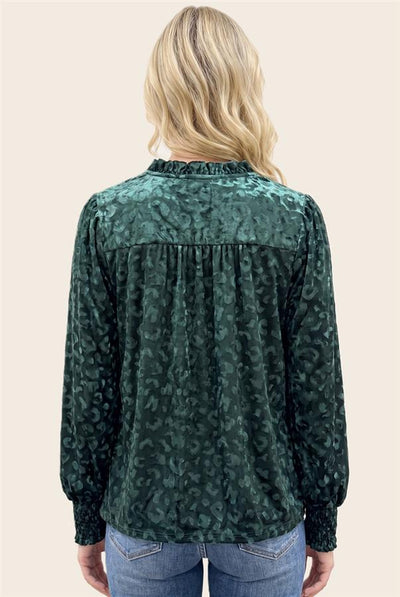Back of a woman wearing a dark green leopard-print long-sleeve blouse and blue jeans, against a solid light beige background.