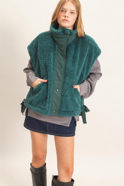 model wearing a gray shirt and jeans skirt with a green Sherpa Vest over it.