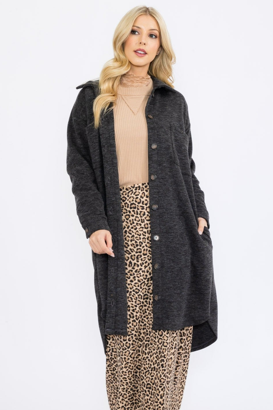 Woman wearing a long dark coat over a beige top and leopard print skirt on a white background