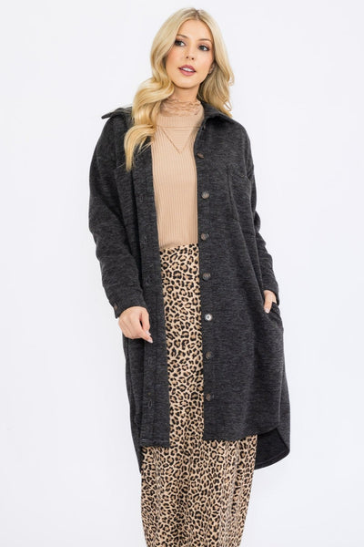 Woman wearing a long dark coat over a beige top and leopard print skirt on a white background