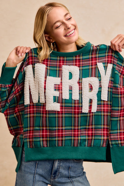 Person wearing a plaid sweater with 'MERRY' text, holding it up.