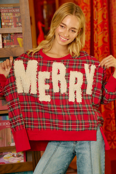 Person wearing a red plaid sweater with 'MERRY' text, standing in a room with books and curtains.