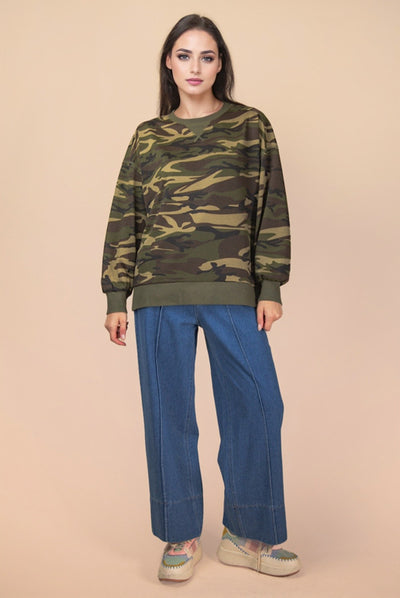 Woman wearing a camouflage sweater and blue pants on a beige background