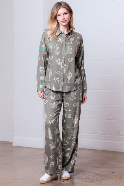 Woman wearing a green pajama set with nature-themed design against a white brick wall.