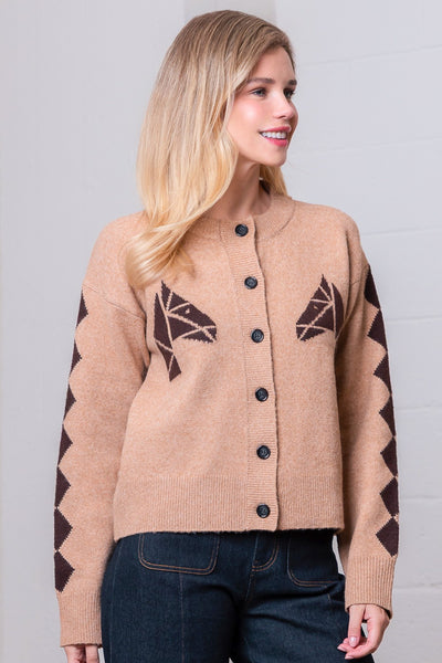 Woman wearing a beige cardigan with brown geometric patterns on a plain background