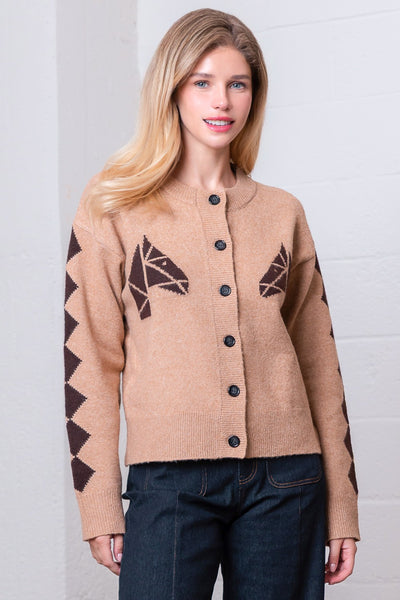 Woman wearing a beige cardigan with brown geometric patterns on sleeves against a white background