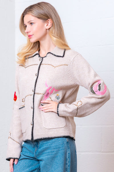 Woman wearing a beige cardigan with colorful designs on a white background