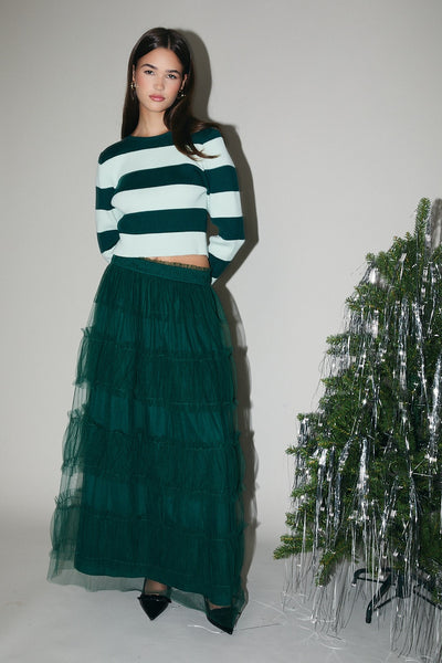 Woman wearing a green and white striped sweater and green skirt standing next to a decorative Christmas tree.