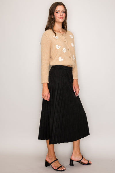 Woman wearing a beige floral cardigan and black skirt against a white background