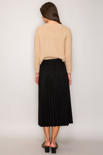 Woman wearing a beige sweater and black skirt against a plain background