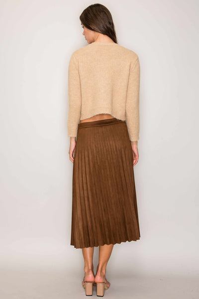Woman wearing a beige cardigan and brown pleated skirt on a plain background