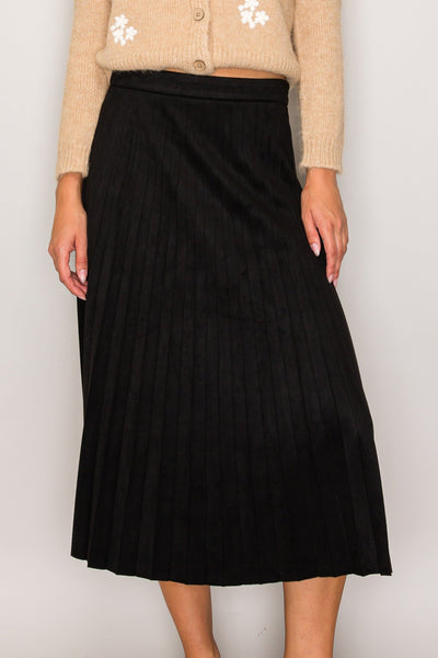 Woman wearing a beige cardigan with floral patterns and a black skirt on a plain background