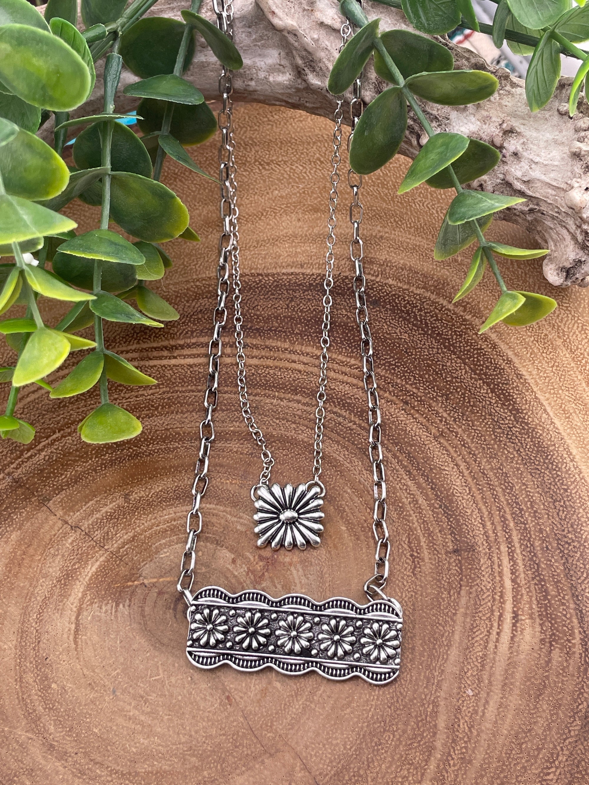 Silver necklace with floral pendant on a wooden surface with green leaves.