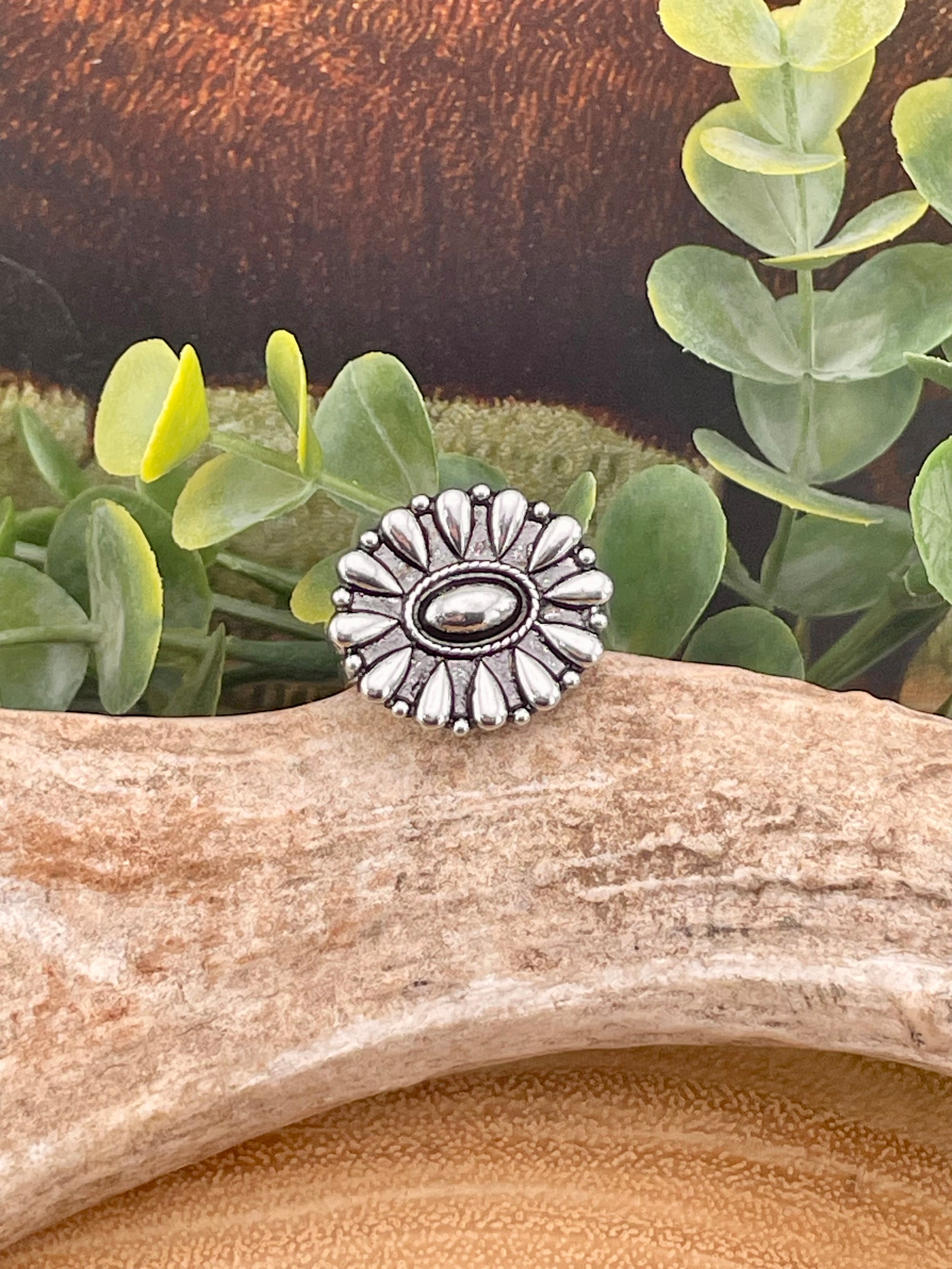 Silver floral-patterned ring on a piece of driftwood with green leaves in the background