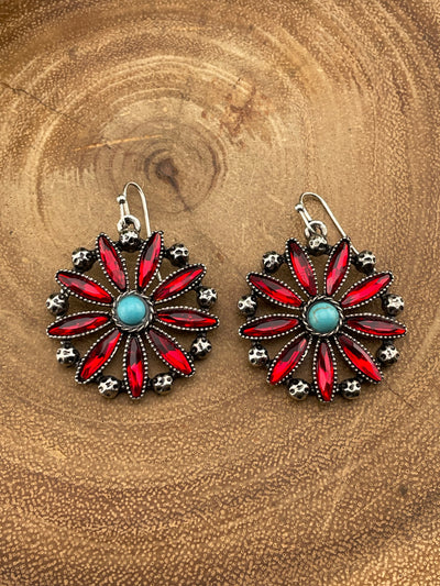 Pair of red floral earrings with a central turquoise stone on a wooden surface