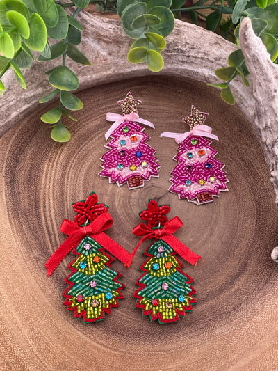 Two pairs of Christmas Tree earrings on a wooden surface with greenery around