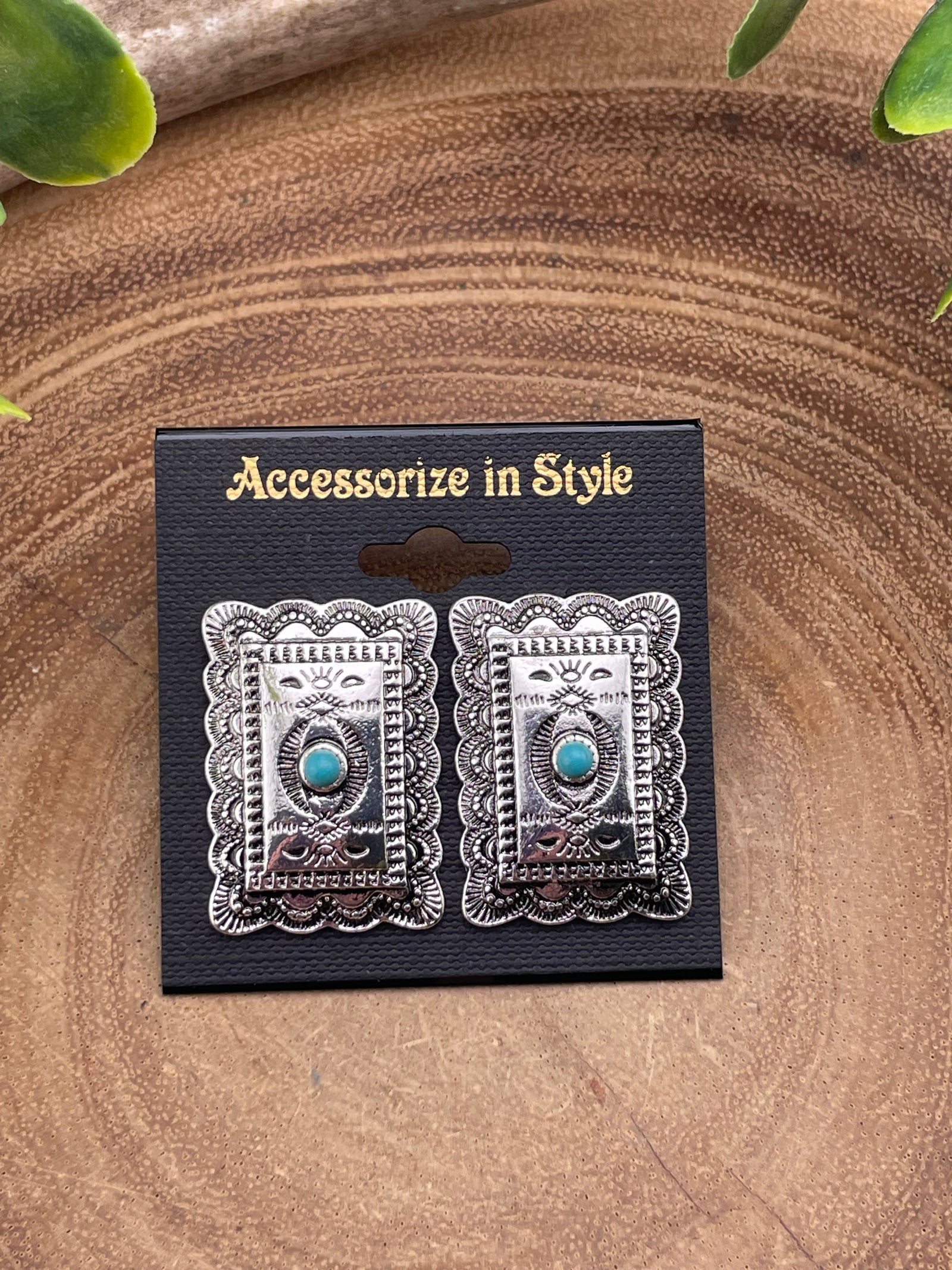 Pair of silver earrings with turquoise stones on a black card with 'Accessorize in Style' text, placed on a wooden surface.
