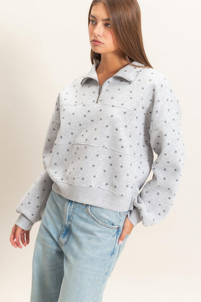 model wearing gray half zip sweatshirt with stars and jeans before a light background